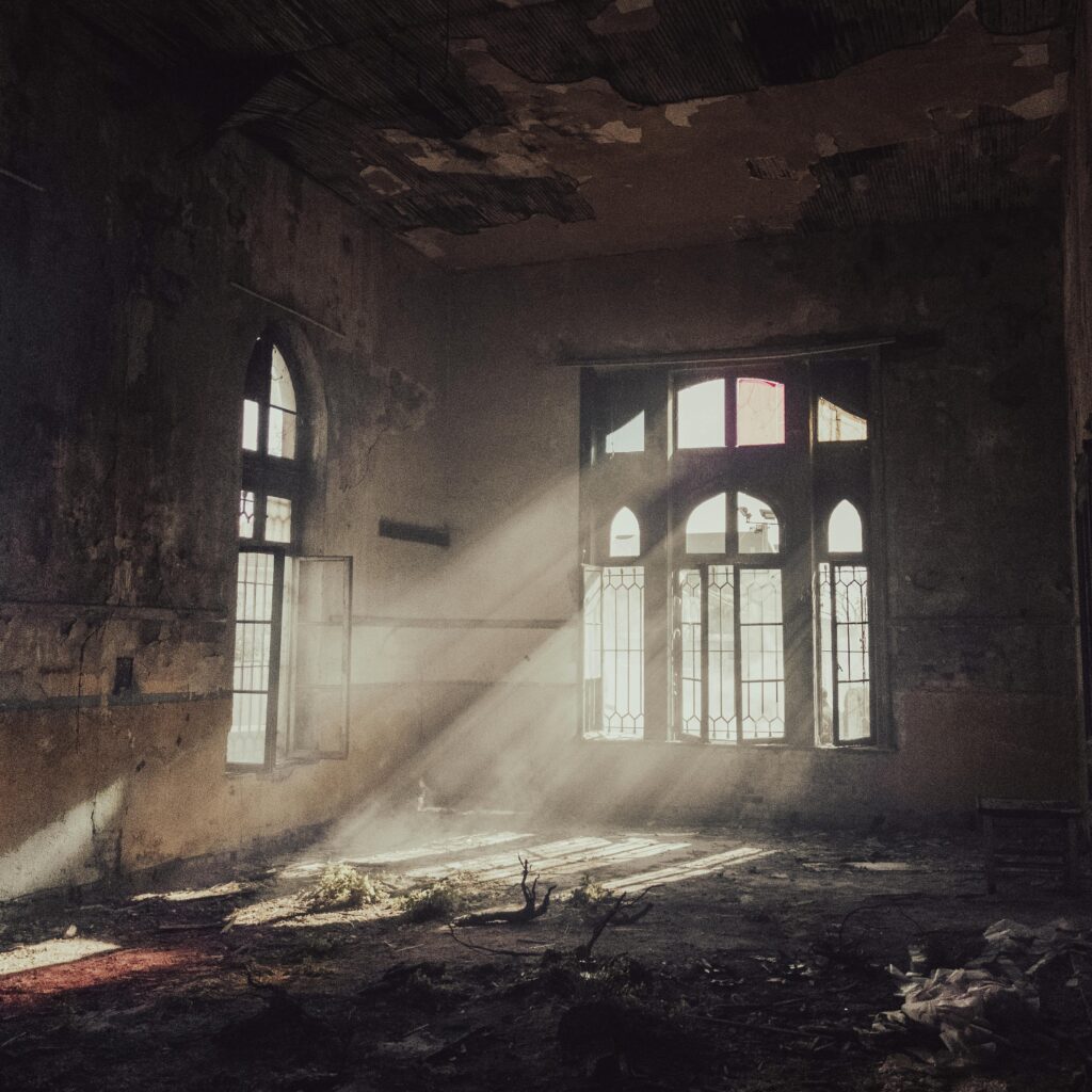 Eerie and abandoned room with sunlight streaming through broken windows, highlighting decay.